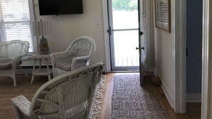 A room with wicker furniture, a flat-screen TV, and a door leading outside. - Beautiful home & short walk to beach, restaurants, and marinas in Rock Hall, MD (Rock Hall)