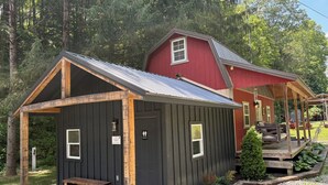 A rustic cabin with a wooden porch and a red barn in the background. - Cabin in Wayne National Forest with ride in/out access to Baileys Trail System (Millfield)