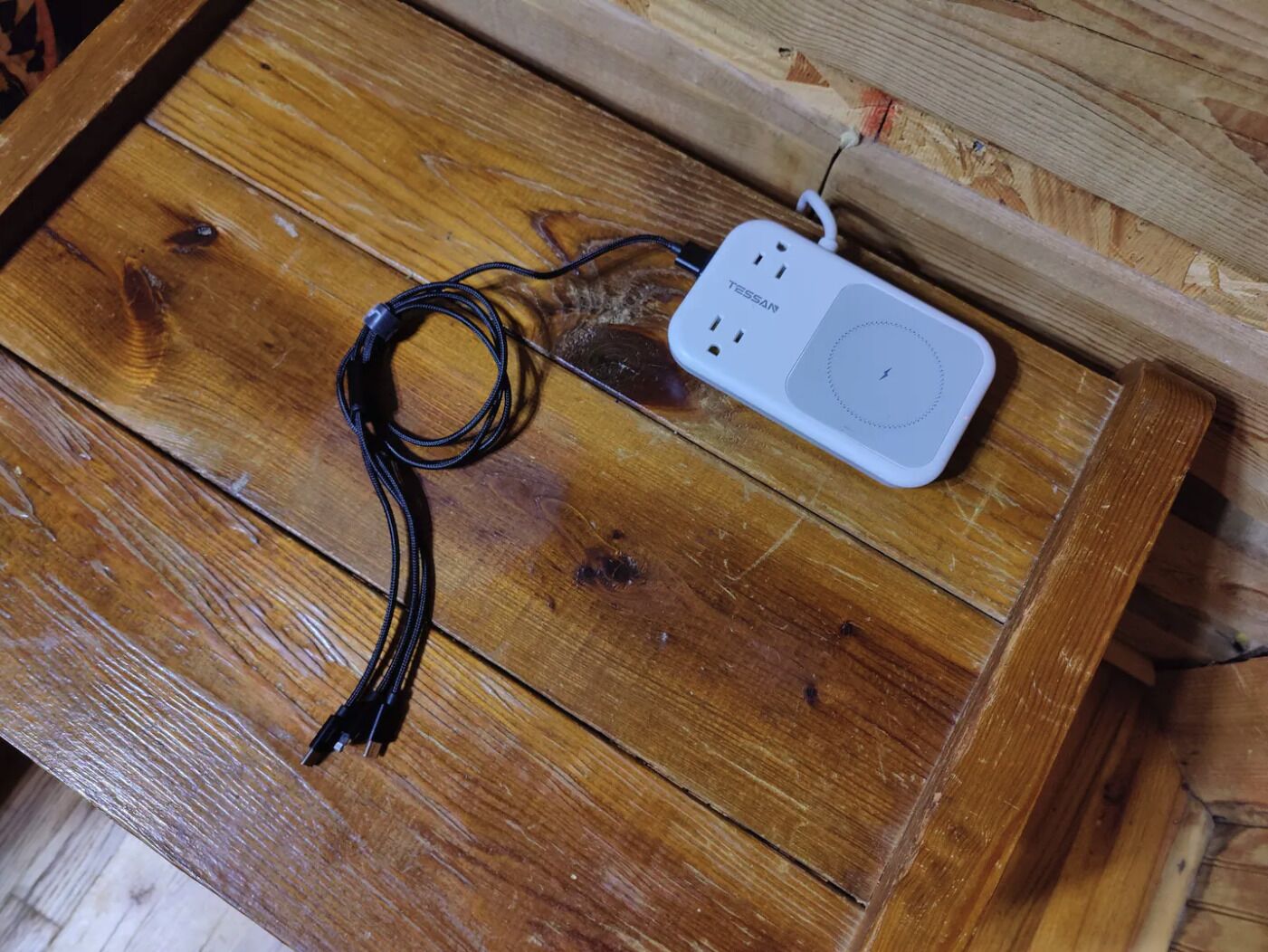 A white power strip with multiple outlets and a USB port on a wooden table.