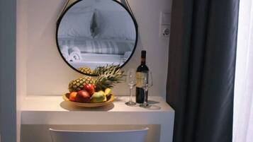 Una habitación de hotel con un espejo redondo, un frutero y una botella de vino sobre una mesa blanca.
