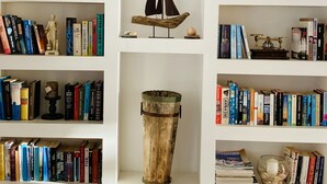 Una estantería con libros, un modelo de velero, un barril de madera y un tablero de ajedrez.