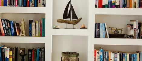 Una estantería con libros, un modelo de velero, un barril de madera y un tablero de ajedrez.