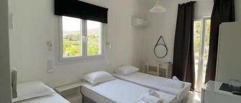 A room with two single beds, a small table, a chair, a desk, and a window with curtains.