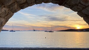 Un arco de piedra con vista al mar tranquilo, con barcos y una puesta de sol.