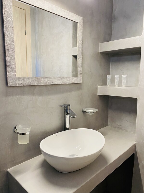 A modern bathroom with a white sink, a large mirror, and a shelf with toiletries.