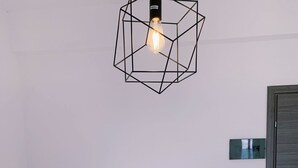 Una cama bien tendida con edredón blanco, dos lámparas de noche, una lámpara colgante de diseño geométrico y una puerta de madera.