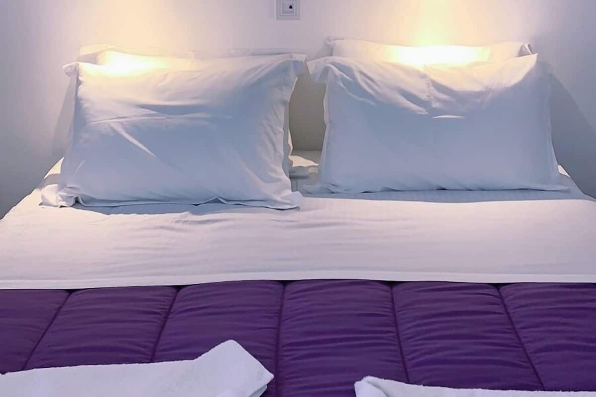 A hotel room with a bed, two bedside tables, and a purple bedspread.