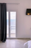 A room with a view of the sea through a sliding glass door, a bed, and a flat-screen TV mounted on the wall.