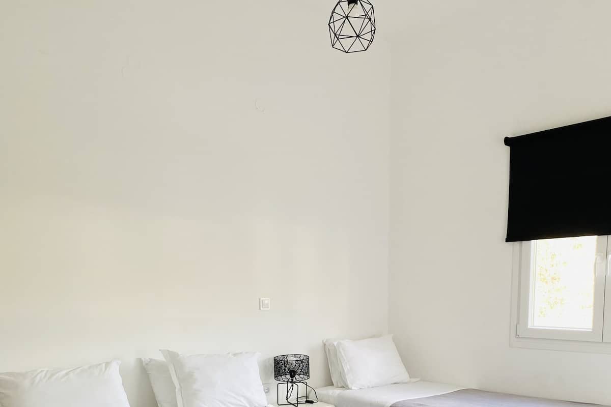 A bedroom with two beds, a nightstand, a lamp, and a window with a blind.