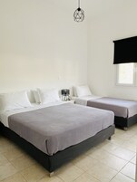 Slaapkamer met twee bedden, een nachtkastje, een lamp en een raam met een jaloezie.