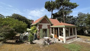 Une maison à deux étages avec un toit recouvert de tuiles rouges, une véranda et un petit jardin.
