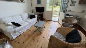 Un salon comprenant un canapé, une table basse, un fauteuil en osier, un téléviseur et une porte-fenêtre coulissante donnant sur un espace extérieur.