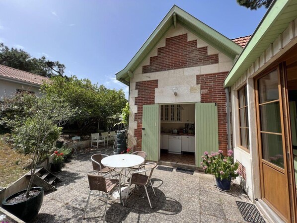 Una casa con fachada de ladrillo, puerta verde y un pequeño patio con mesa y sillas.