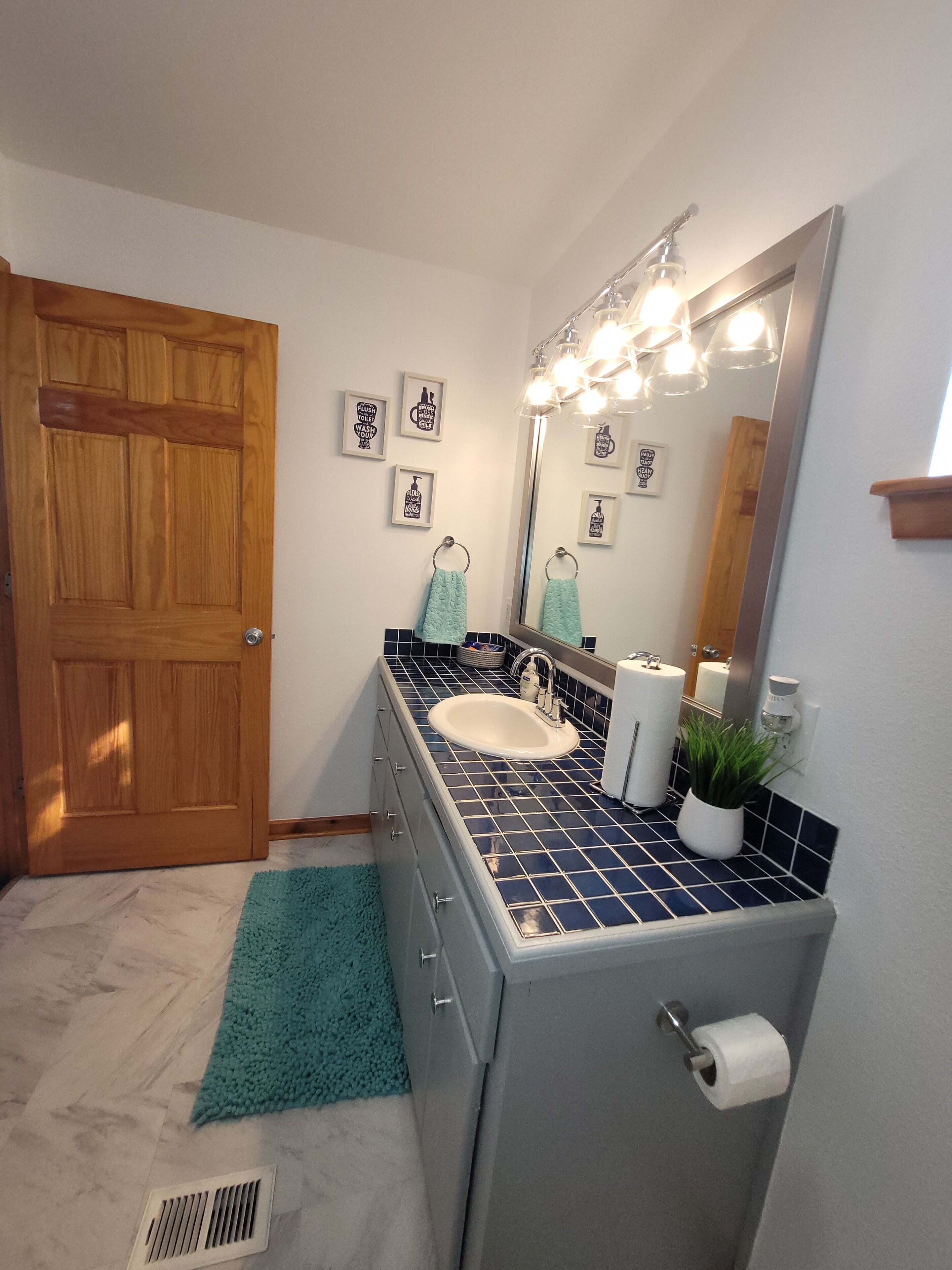 Un baño con puerta de madera, un lavabo con espejo y un revestimiento de azulejos azules.