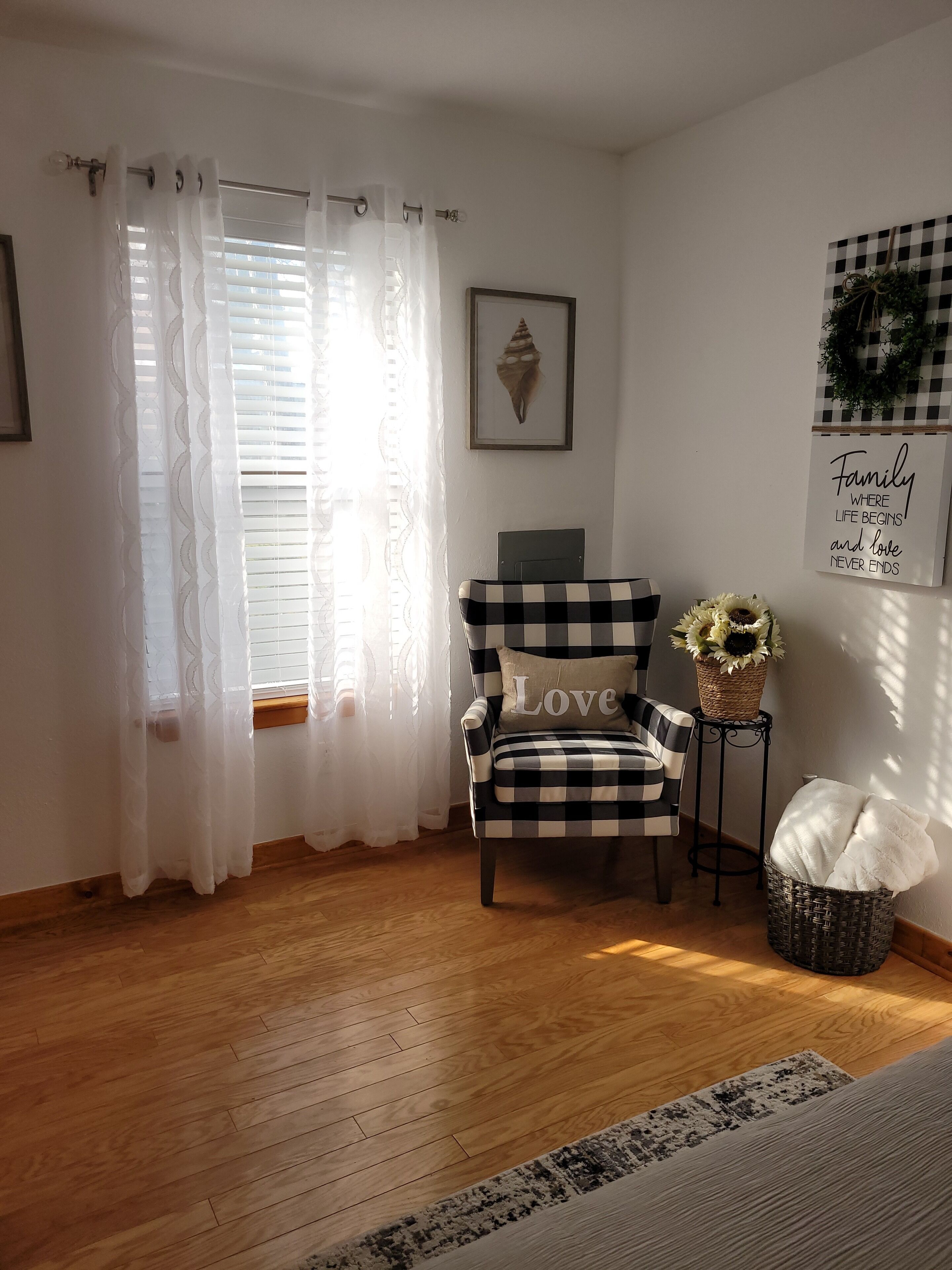Una habitación con un sillón a cuadros, una cita enmarcada en la pared y una cesta con una planta.