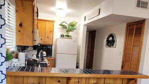 A kitchen with wooden cabinets, a black countertop, two bar stools, a refrigerator, and a potted plant. - Modern meets Rustic Cabin on the Lake (Livingston)