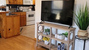 A modern kitchen with wooden cabinets, a microwave, and a stove. There is a TV on a wooden stand with shelves holding decorative items and plants. - Modern meets Rustic Cabin on the Lake (Livingston)