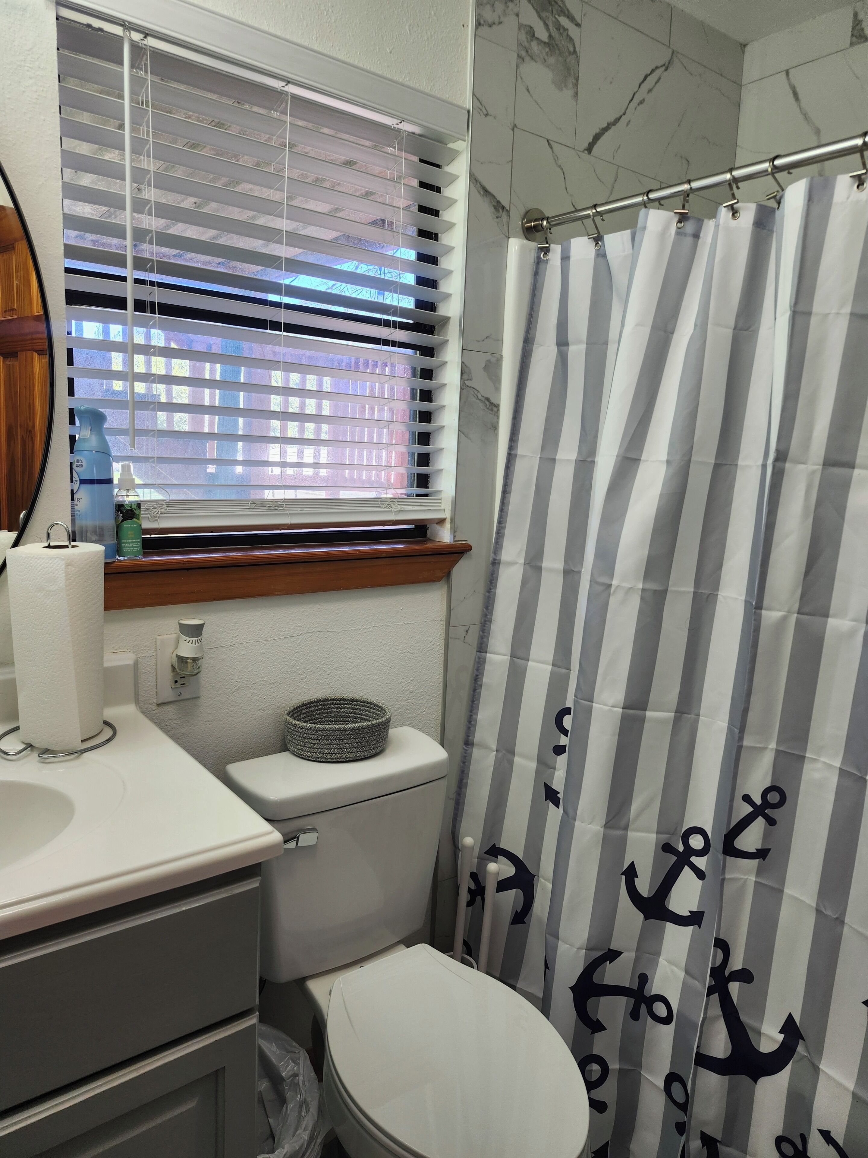 Une salle de bain comprenant des toilettes, un lavabo, une fenêtre avec stores et un rideau de douche à rayures.