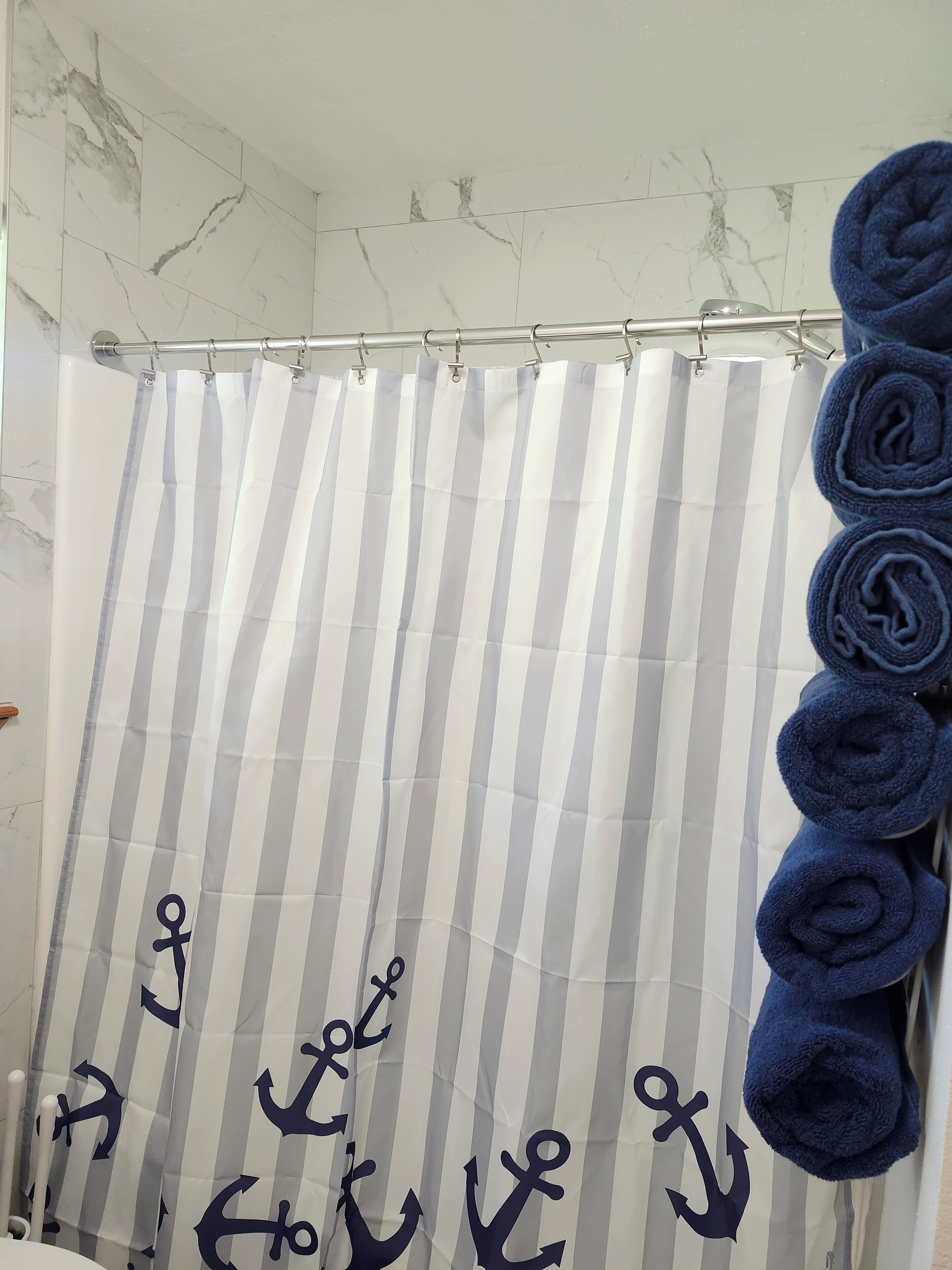 A bathroom with a striped shower curtain, a metal shower rod, and rolled towels on a rack.