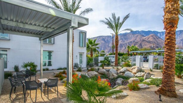 Une terrasse extérieure moderne, aménagée avec des sièges, des palmiers et offrant une vue sur les montagnes.
