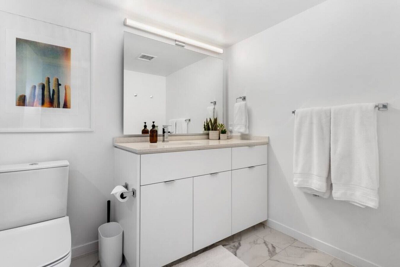 Ein modernes Badezimmer mit einem weißen Waschtisch, einem großen Spiegel und einem Handtuchhalter.