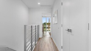 Un couloir moderne avec un plancher en bois, des murs blancs et un portail en métal.