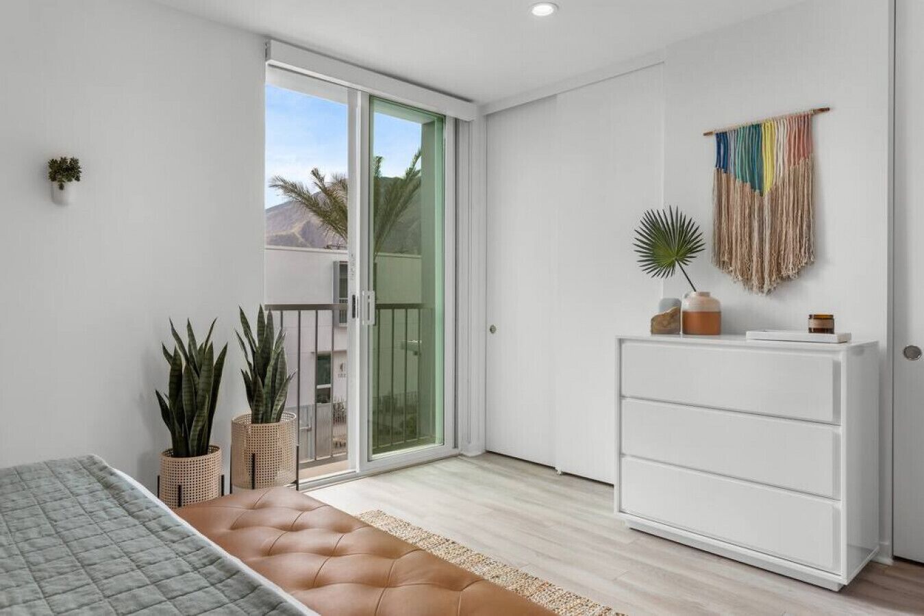 A modern bedroom with a bed, a dresser, and potted plants.