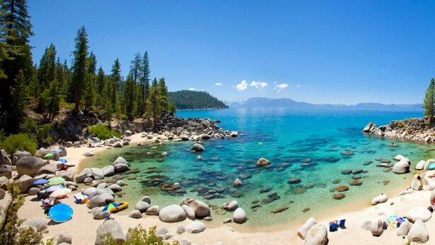 Ein Strand mit klarem türkisblauem Wasser, umgeben von Felsen und Bäumen.