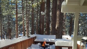Ein mit Schnee bedeckter Deck mit Feuerstelle, umgeben von hohen Bäumen.