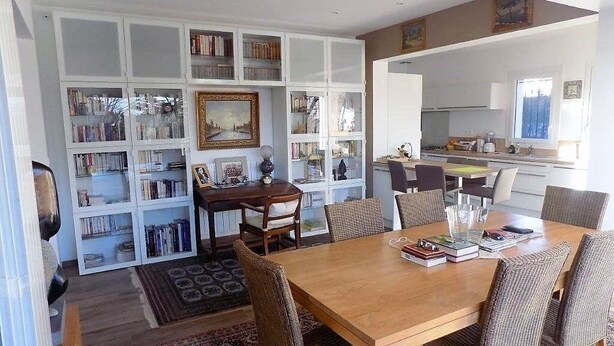 A dining area with a wooden table and wicker chairs, surrounded by white bookshelves filled with books. - Saint Palais sur Mer - BEAUTIFUL RENOVATED HOUSE – HEATED POOL – EVERYTHING ON FOOT (ST PALAIS SUR MER)