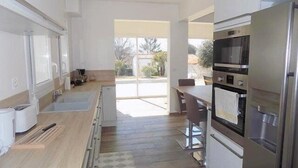 A modern kitchen with stainless steel appliances, a dining area with a table and chairs, and a view through the glass door. - Saint Palais sur Mer - BEAUTIFUL RENOVATED HOUSE – HEATED POOL – EVERYTHING ON FOOT (ST PALAIS SUR MER)