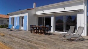 A modern house with a patio area featuring a table and chairs, a covered seating area with lounge chairs, and a large sliding glass door. - Saint Palais sur Mer - BEAUTIFUL RENOVATED HOUSE – HEATED POOL – EVERYTHING ON FOOT (ST PALAIS SUR MER)