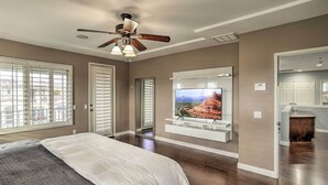 A bedroom with a bed, a ceiling fan, a TV mounted on the wall, and a view of the outside. - Spacious Indio Home: Pool, Grill, & Fire Pits (Indio)