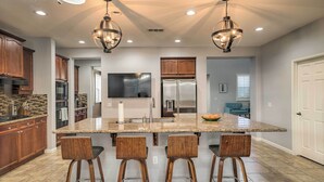 A spacious kitchen with granite countertops, wooden bar stools, and stainless steel appliances. - Spacious Indio Home: Pool, Grill, & Fire Pits (Indio)