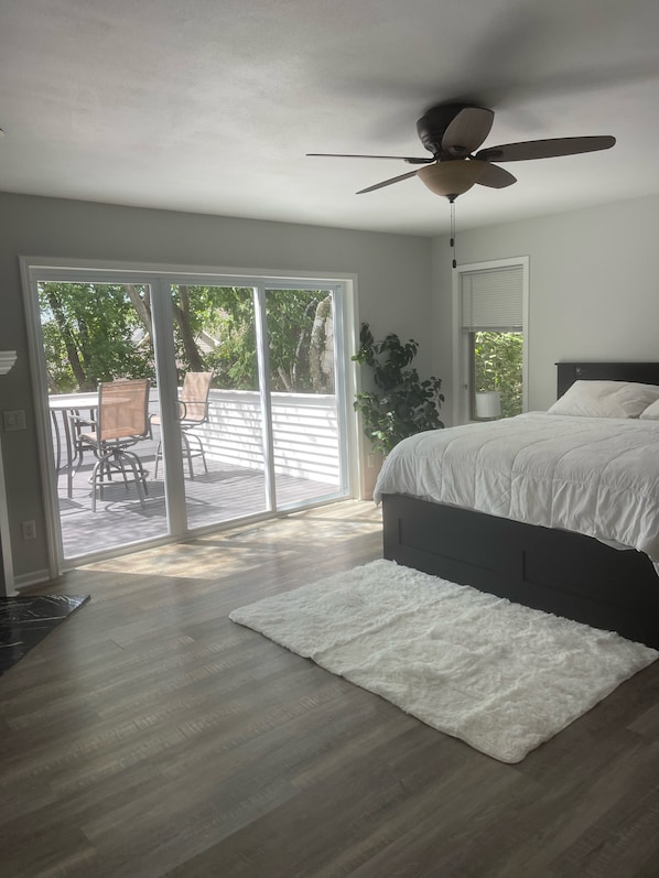 A bedroom with a large bed, a ceiling fan, and a view through a sliding glass door to an outdoor patio.
