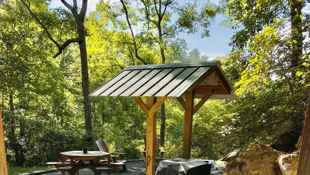 Ein Whirlpool, umgeben von einer Holterrasse, mit einer Pergola und einem Picknicktisch im Hintergrund.