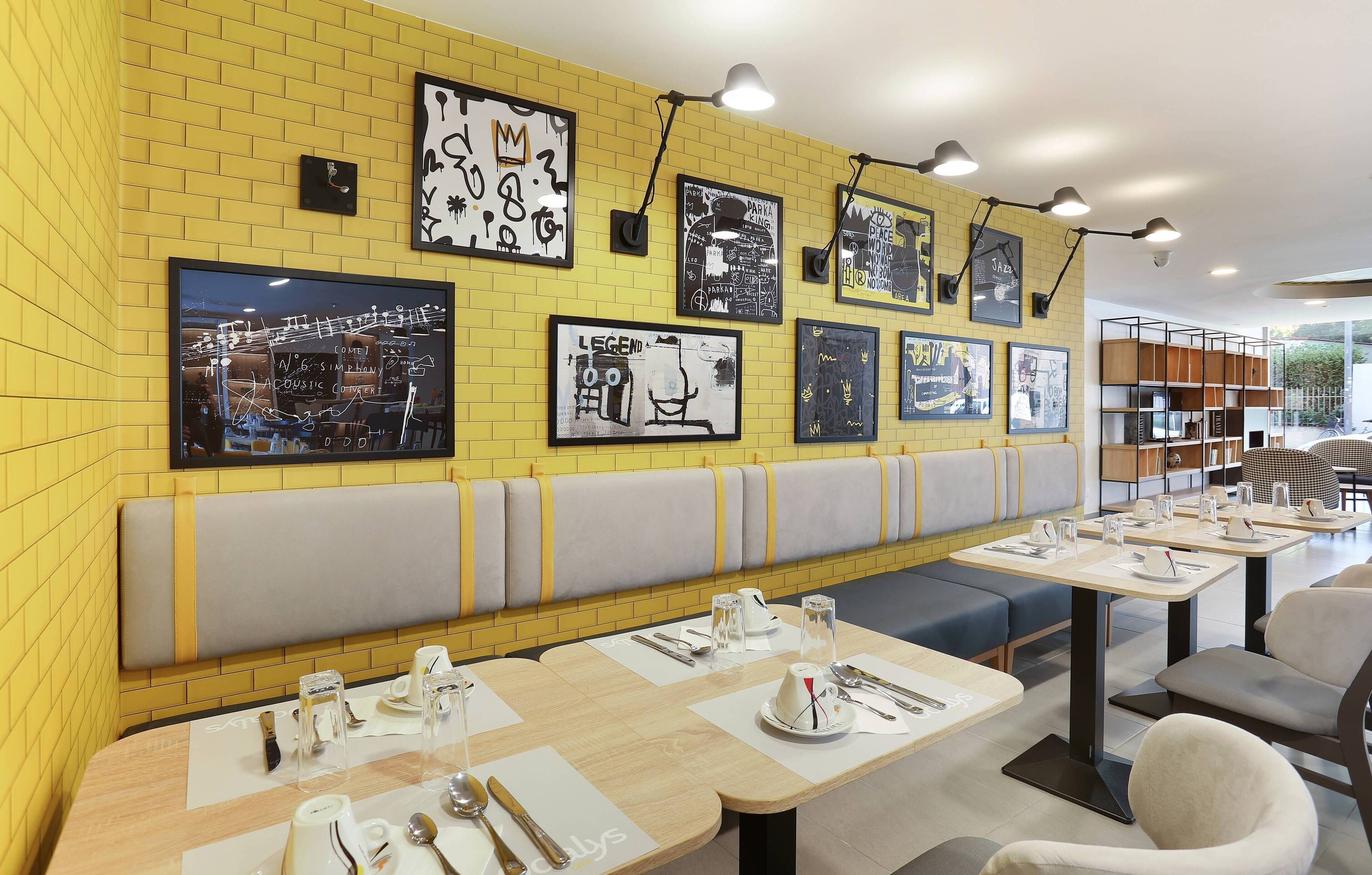 Een restaurant met geel bakstenen muren, kunstwerken en moderne zitplaatsen. Tafels zijn gedekt met bestek en glazen.