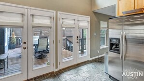Une cuisine équipée d’un réfrigérateur en acier inoxydable, de meubles blancs et d’un espace patio visible à travers des portes vitrées.