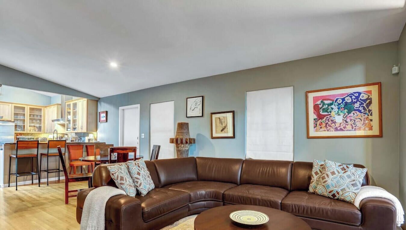 A living room with a brown leather sofa, a round coffee table, and a dining area with wooden chairs and a table.