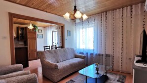 A living room with a sofa, armchairs, a glass coffee table, and a television.