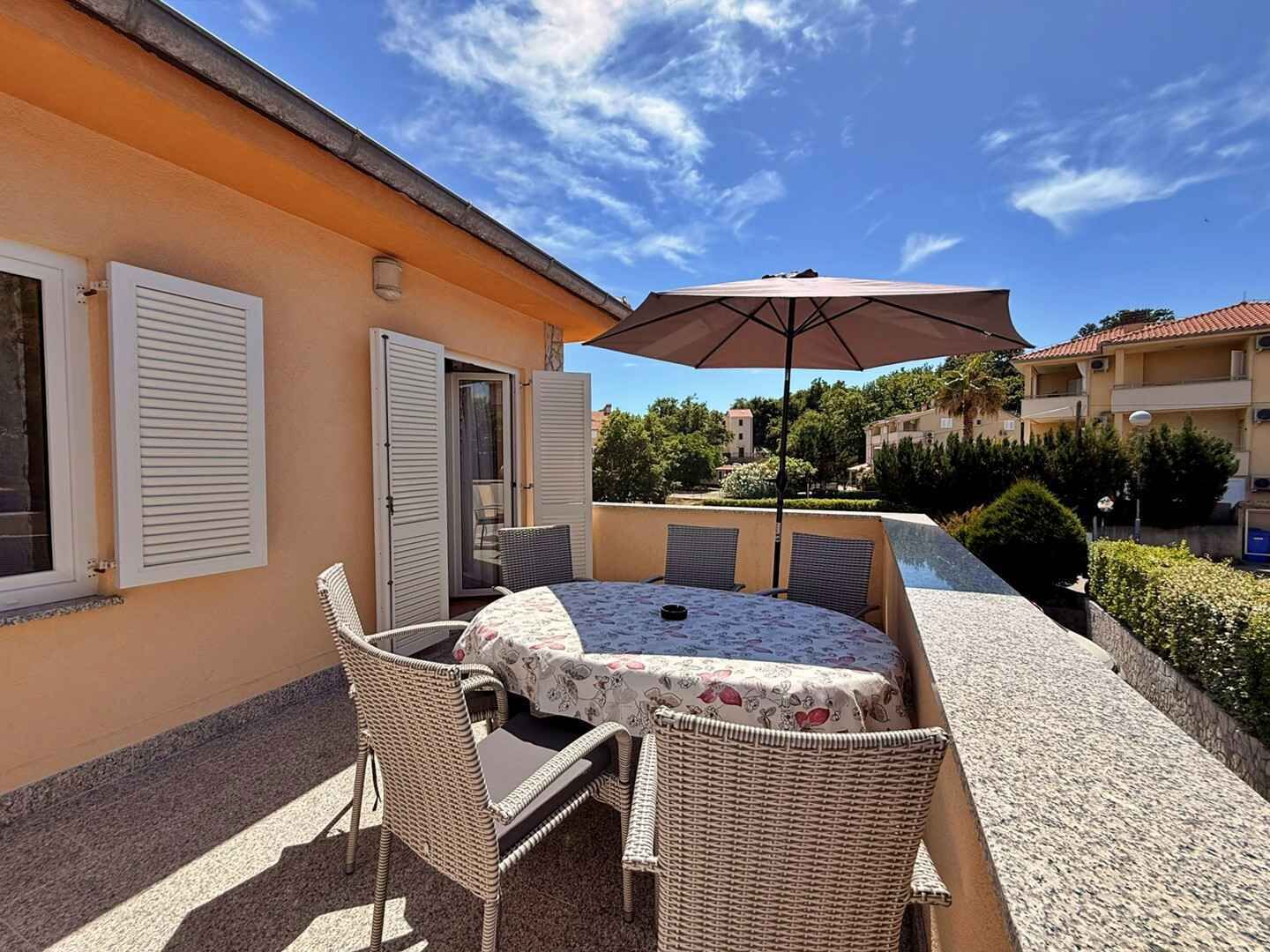 An outdoor patio with a round table and chairs, a table umbrella, and a pool in the background.