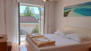 A bedroom with a bed, a painting of a beach, and a balcony with a railing.