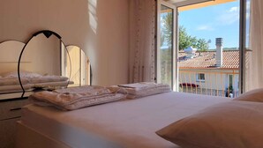 A bedroom with a bed, a bedside table, a mirror, and a view of the outside.