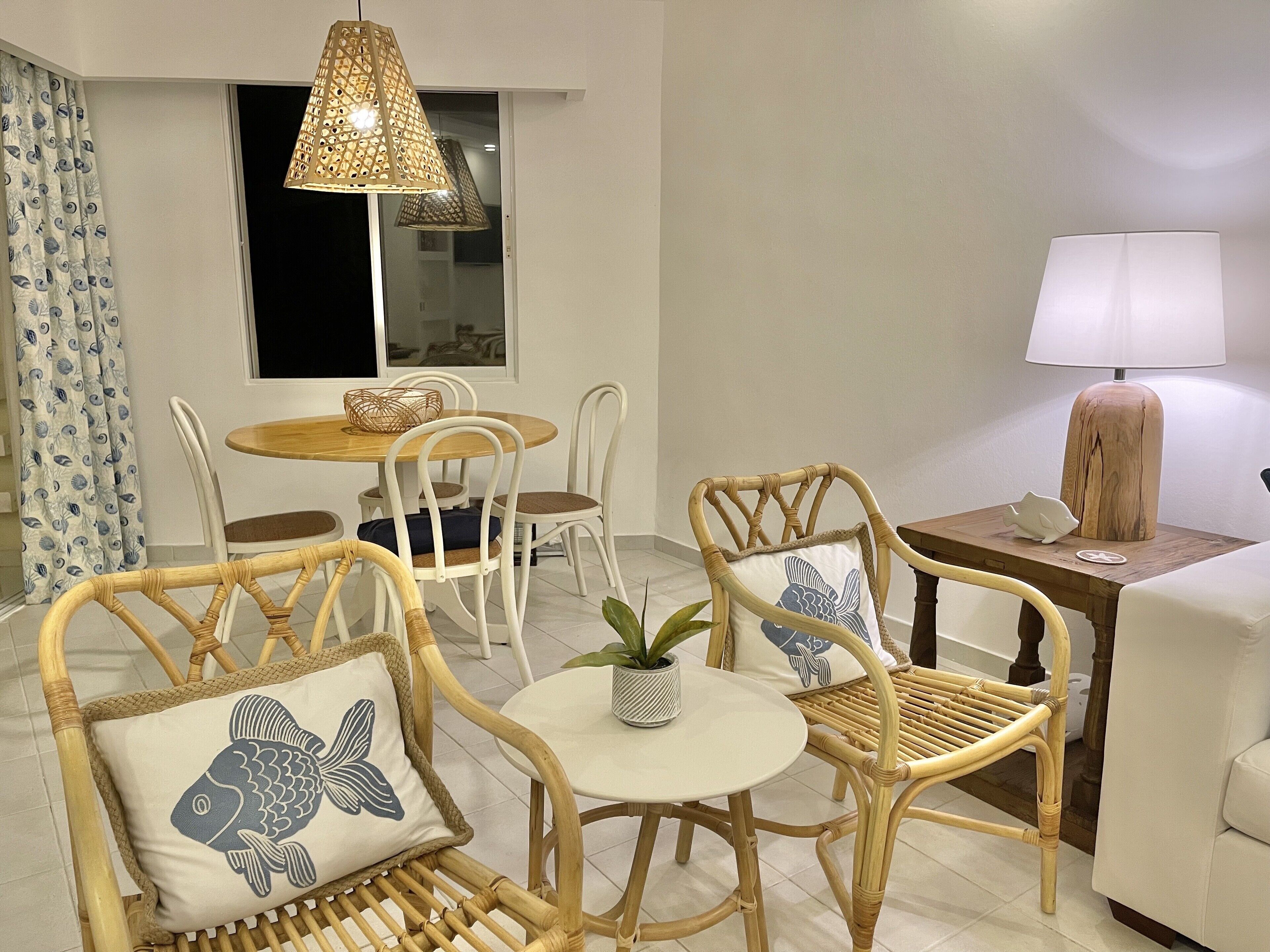A room with a dining table, four chairs, a small side table with a lamp, and a sofa.