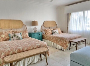 Une chambre d’hôtel avec deux lits, une petite table, un banc et une fenêtre avec des rideaux.