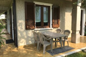 Une terrasse couverte avec une table et des chaises, une fenêtre avec des volets et un pilier en béton.