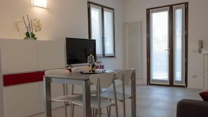 Ein moderner Essbereich mit Tisch, Stühlen, einem Fernseher und einer Vase mit Blumen.