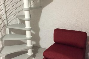 Un coin de pièce avec un escalier en colimaçon blanc et une chaise rouge.