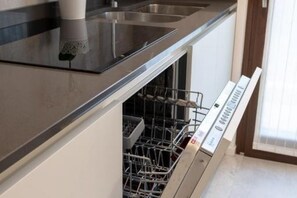 Une cuisine dotée de plans de travail en acier inoxydable, d’un lave-vaisselle et d’une fenêtre avec des stores.