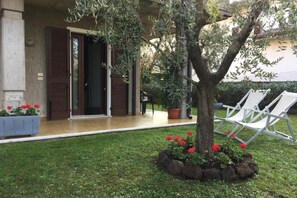 Un bâtiment doté d’un porche couvert, un arbre aux fleurs rouges et des chaises longues blanches.